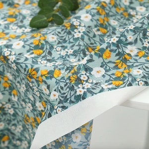 May include: A close-up of a light blue fabric with a white and yellow floral pattern. The fabric is waterproof and has a subtle sheen.