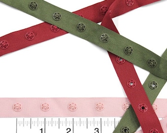 May include: Three different colours of snap tape with plastic snaps. The tape is shown on a white surface with a ruler in the bottom of the image. The ruler shows measurements in inches.