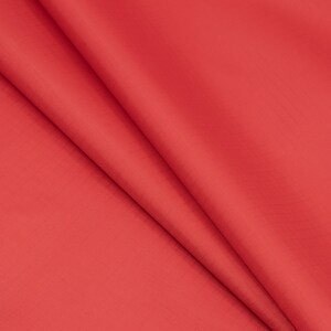 May include: A close-up shot of a vibrant red fabric with subtle folds. The material has a smooth texture and a slight sheen, suggesting it might be a satin or similar type of cloth. The folds create shadows and depth, highlighting the fabric's drape.