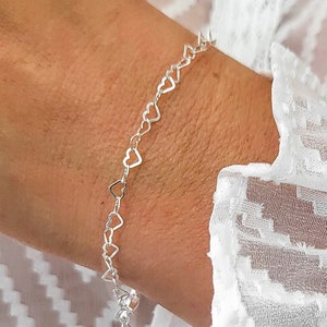 Könnte beinhalten: Ein silbernes Armband mit einer zarten Kette aus miteinander verbundenen Herzformen.