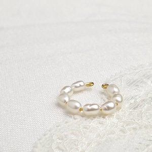 Op de afbeelding: Een gouden oorring met een rij witte parels. De oorring is open en heeft een eenvoudig ontwerp.