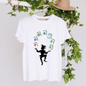 May include: White t-shirt with a black silhouette of a person juggling mahjong tiles. The tiles have Chinese characters for North, South, East, West, and Center.