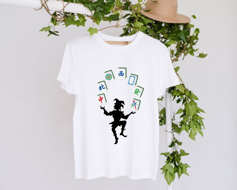 May include: White t-shirt with a black silhouette of a person juggling mahjong tiles. The tiles have Chinese characters for North, South, East, West, and Center.