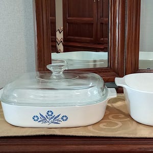 May include: Two white ceramic baking dishes with blue floral designs. One dish has a glass lid.