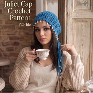 Puede incluir: Un gorro Juliet de ganchillo azul con detalles de perlas y largas borlas. El texto "The Juliet Cap Crochet Pattern PDF file" está en la imagen. Una persona lleva el gorro y sostiene una taza de té.