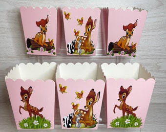May include: Six pink paper treat boxes with scalloped edges. Each box features a Bambi cartoon illustration with butterflies, flowers, and woodland creatures. The boxes are displayed on a clear acrylic stand.