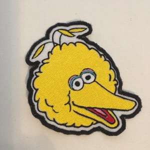 Puede incluir: Parche bordado con Big Bird de Barrio Sésamo. El parche tiene un cuerpo amarillo, un pico largo amarillo y ojos grandes con detalles en rosa y azul. El parche está contorneado en negro.