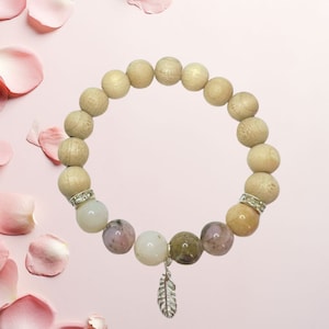 Könnte beinhalten: Ein Armband aus Holzperlen mit einem silbernen Federschmuck. Das Armband besteht aus hellbraunen Holzperlen und verschiedenen bunten Edelsteinperlen, darunter rosa, weiße und grüne.