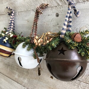 Op de afbeelding: Drie kerstbelletjes met verschillende kleuren verf en stervormige uitsnijdingen. De belletjes zijn versierd met groen en kleine witte bessen.