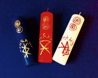 May include: Three candles with gold and red markings. The candles are blue, red, and white. The blue candle has a gold symbol and the text "OCHRA". The red candle has a gold symbol and the text "IST". The white candle has a gold symbol and the text "STAX".