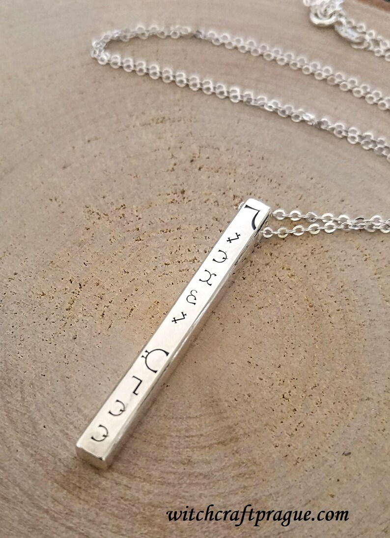 May include: A silver bar necklace with a chain and a pendant engraved with astrological symbols. The pendant is engraved with the symbols for the sun, moon, Mercury, Venus, Mars, Jupiter, Saturn, Uranus, Neptune, and Pluto.