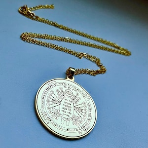 May include: Gold-colored pendant necklace with a circular charm. The charm features intricate engraved symbols and text, with a detailed design. The necklace chain is also gold-colored, and the pendant hangs from it. The background is a solid light blue.