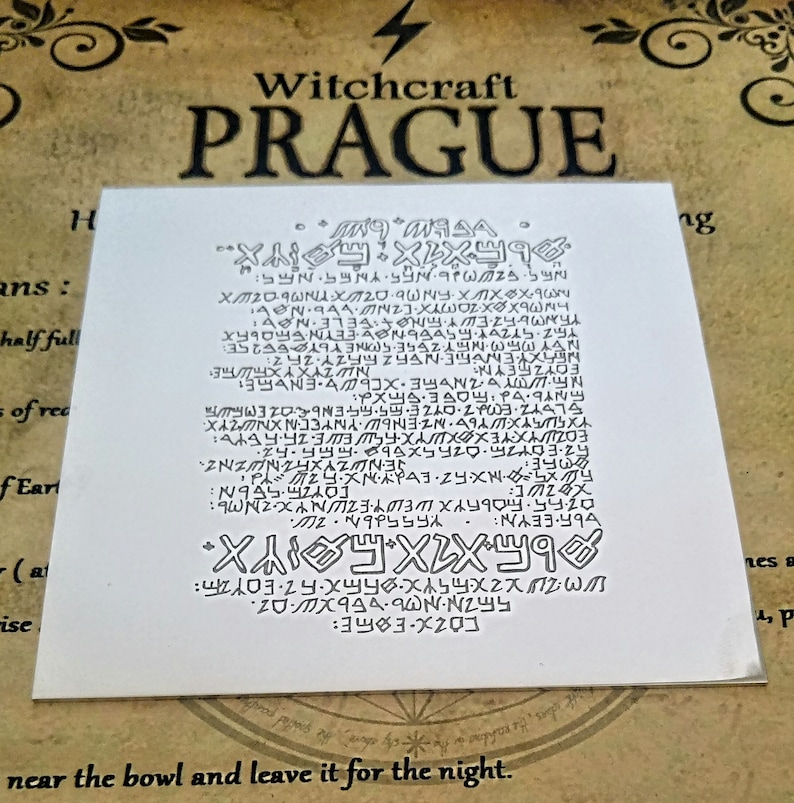 May include: A white card with black text and symbols. The text reads "Witchcraft Prague" and includes a series of symbols and letters. The text at the bottom reads "near the bowl and leave it for the night."
