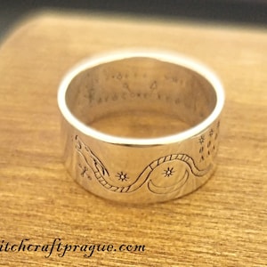 May include: A silver ring featuring an intricate design of a snake coiled around a crescent moon and stars. The ring is engraved with the words "Free Your Spirit".