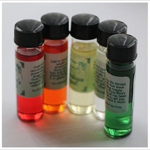 May include: Five small glass bottles with black caps filled with different colored liquids. The bottles have labels with text that includes the words "Used to bring", "Said to bring", "Guardian", "Life throws", and "Anna Riva's".
