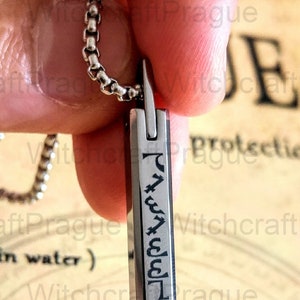 May include: A silver necklace with a silver pendant featuring a vertical inscription of symbols. The pendant is rectangular and has a smooth, polished surface.