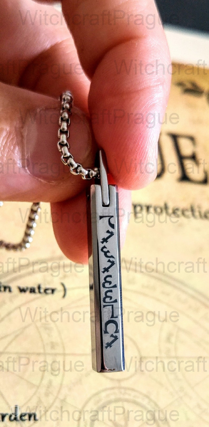 May include: A silver necklace with a silver pendant featuring a vertical inscription of symbols. The pendant is rectangular and has a smooth, polished surface.