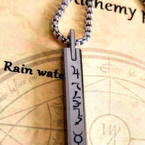 May include: A silver chain necklace with a silver pendant. The pendant is rectangular and has a symbol on it. The symbol is a combination of letters and symbols. The necklace is lying on a piece of paper with a map on it.
