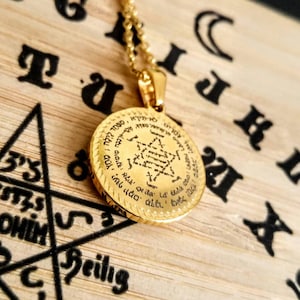 May include: A gold pendant necklace with a round charm featuring Hebrew text and a Star of David design. The charm is engraved with Hebrew text and a Star of David design.