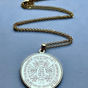May include: Gold-colored pendant necklace with a circular pendant. The pendant features intricate engraved symbols and text, suspended from a delicate chain. The necklace is displayed against a light gray background.
