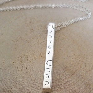 May include: Silver bar necklace with engraved astrological symbols. The symbols include the sun, moon, Mercury, Venus, Mars, Jupiter, Saturn, Uranus, Neptune, and Pluto.