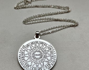 May include: A silver-toned circular pendant necklace featuring intricate black engraved text and geometric patterns. The design includes the words TETRAGRAMMATON, ADONAY, ELOHIM, and SCHAIDE, arranged in concentric circles with various symbols.