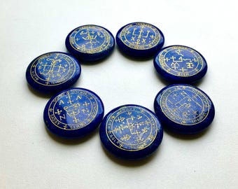 May include: Seven circular, deep blue polished stones arranged in a ring. Each stone features intricate gold-colored engravings of mystical symbols, geometric lines, and various letters including A, N, and Z, along with words like AGLA and SADAY.