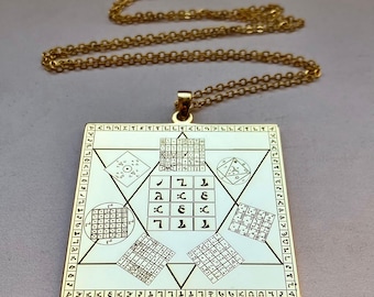 May include: Gold-colored pendant necklace with a square pendant featuring geometric shapes and symbols. The pendant is attached to a delicate gold chain. The design includes a star, squares, and various symbols.
