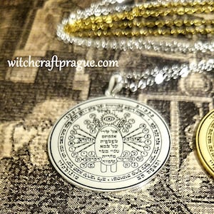 May include: A silver pendant necklace with intricate Hebrew text and symbols. The round pendant features a central design with an eye and various inscriptions. The website witchcraftprague.com is visible in the image. The necklace is displayed on a textured surface.