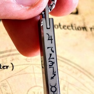 May include: A silver pendant necklace with a rectangular charm featuring a series of symbols and the number 24.