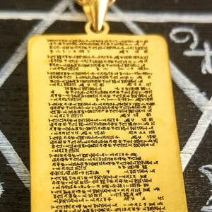 Puede incluir: Un collar de oro con un colgante rectangular que presenta una inscripción detallada en un idioma antiguo. El colgante está unido a una cadena de oro.