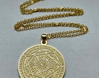 May include: A gold-toned circular pendant necklace featuring an intricate engraved design. The pendant displays a central star pattern surrounded by text including names like Michael, Gabriel, Raphael, and Samael, suspended on a matching gold chain.