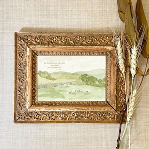 Pode incluir: Uma impressão em aquarela emoldurada com uma cena pastoral com ovelhas pastando em um campo verde. A impressão está dentro de uma moldura dourada ornamentada. O texto "My sheep hear my voice and I know them, and they follow me" é visível.