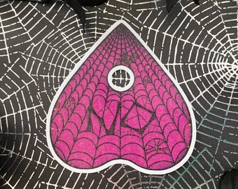 May include: Pink and black heart-shaped sticker with a spiderweb design. The sticker has a hole in the center and the word "YES" written inside.