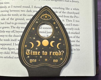 May include: Black and gold ouija board bookmark with a crescent moon and star design. The bookmark has a window with the text "Time to read?" and the words "yes" and "no" below it.