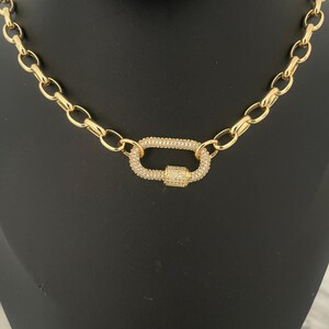 Pu&ograve; includere: Una collana color oro con una grande chiusura di forma ovale. La chiusura e gli anelli di collegamento della catena sono in metallo dorato. La chiusura &egrave; incastonata con piccoli cristalli trasparenti, che aggiungono brillantezza al gioiello.