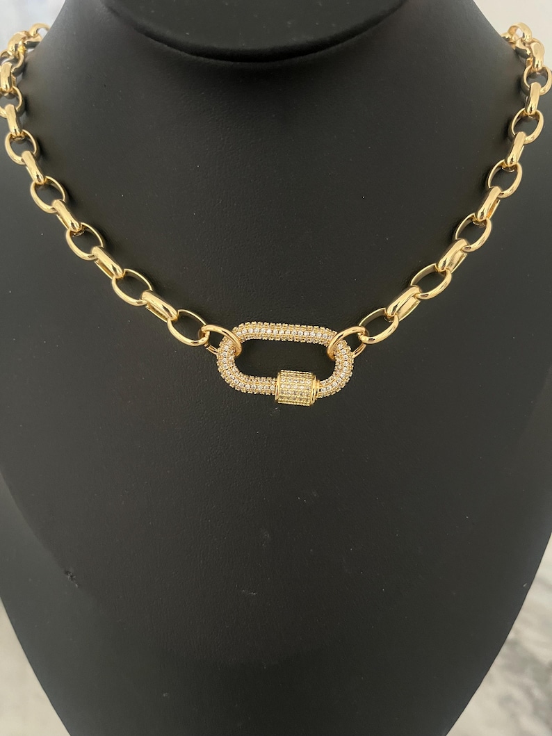 Pu&ograve; includere: Una collana color oro con una grande chiusura di forma ovale. La chiusura e gli anelli di collegamento della catena sono in metallo dorato. La chiusura &egrave; incastonata con piccoli cristalli trasparenti, che aggiungono brillantezza al gioiello.