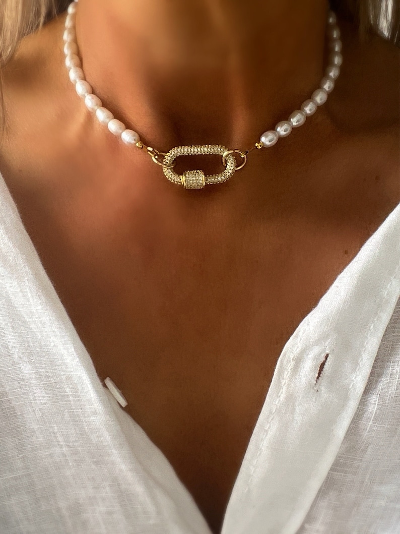May include: A gold necklace with a large, sparkly, oval-shaped clasp and a strand of white pearls.