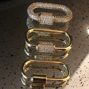 May include: Three gold-toned metal clasps with a cylindrical design. The clasps are adorned with clear cubic zirconia stones.