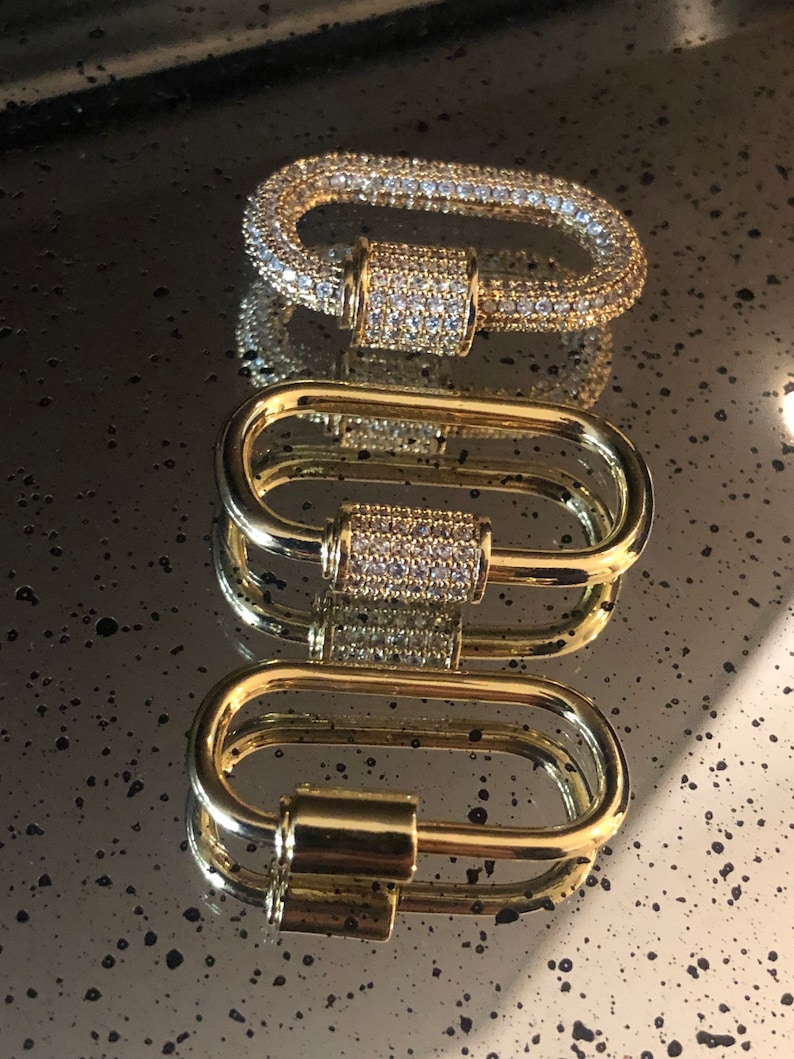 May include: Three gold-toned metal clasps with a cylindrical design. The clasps are adorned with clear cubic zirconia stones.