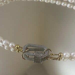 May include: A double strand pearl necklace with a gold and silver clasp encrusted with clear rhinestones.