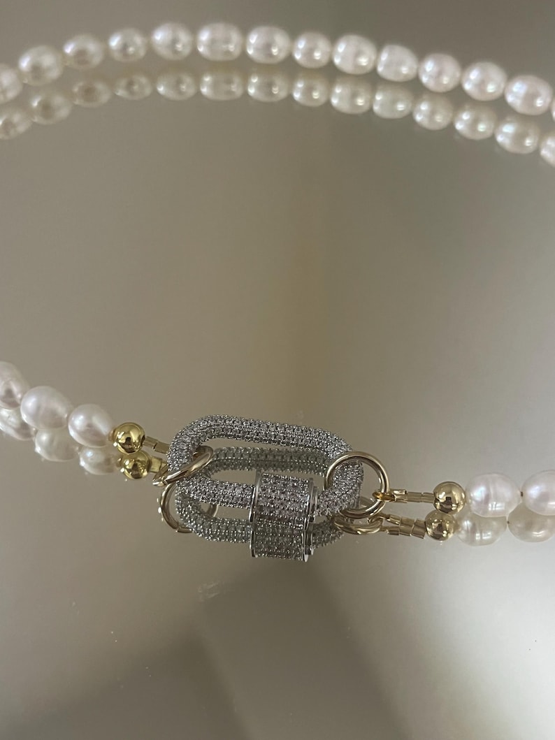 May include: A double strand pearl necklace with a gold and silver clasp encrusted with clear rhinestones.