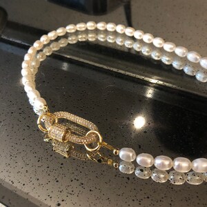 May include: A double strand pearl necklace with a gold clasp encrusted with clear rhinestones.