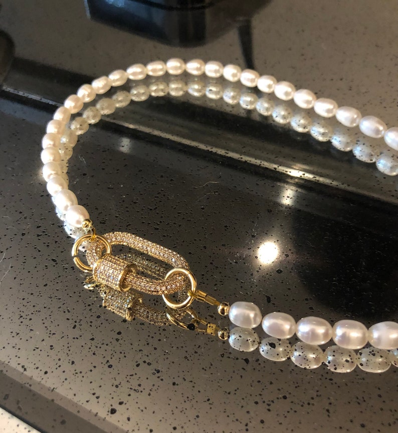 May include: A double strand pearl necklace with a gold clasp encrusted with clear rhinestones.