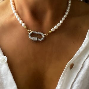 May include: A white pearl necklace with a silver and gold clasp featuring a pave diamond design.