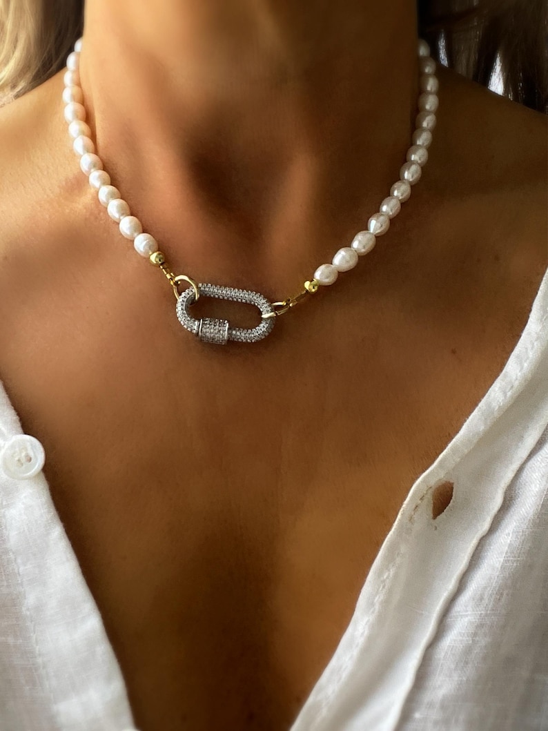 May include: A white pearl necklace with a silver and gold clasp featuring a pave diamond design.