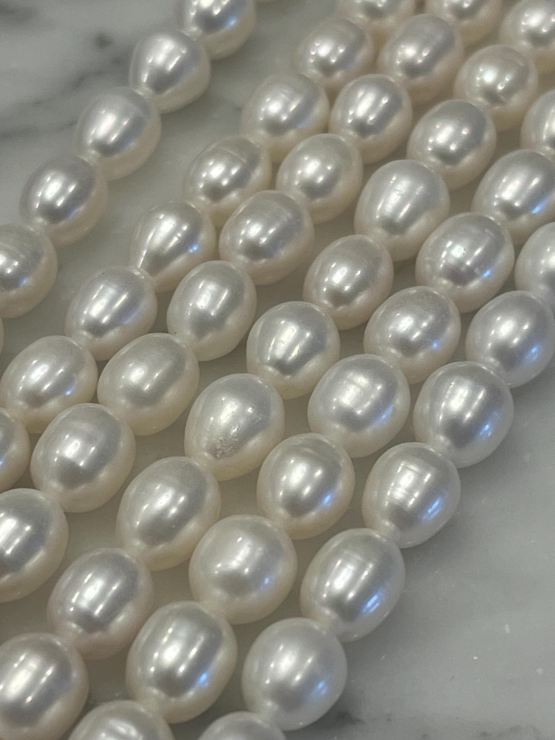 May include: A strand of white pearl beads, arranged in rows, showcasing their smooth, lustrous surface.