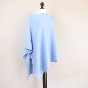 Könnte beinhalten: Ein hellblauer Strickponcho, der über einer Schaufensterpuppe drapiert ist. Der Poncho ist aus einem weichen, leichten Stoff gefertigt und hat ein schlichtes, elegantes Design.