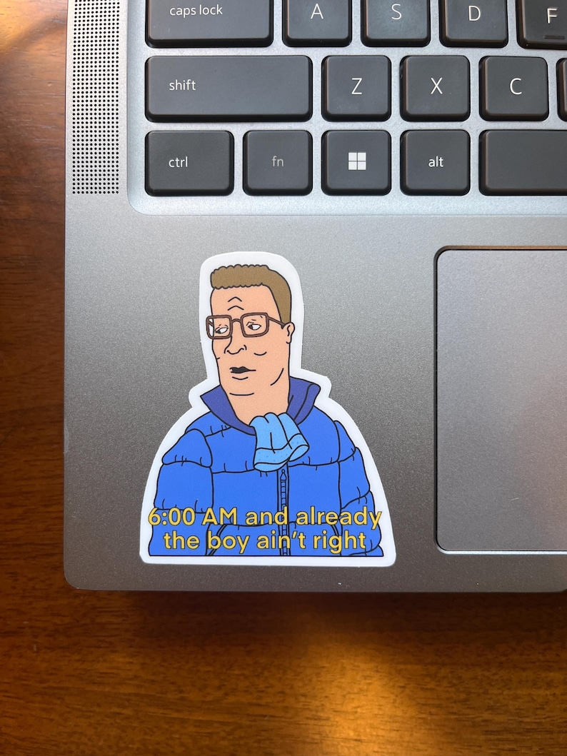 May include: A sticker featuring a cartoon character with a blue jacket and a scarf, with the text "6:00 AM and already the boy ain't right".