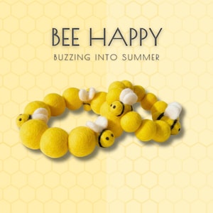 May include: A circular garland made of yellow felt balls and small felt bees with white wings and black stripes. The text BEE HAPPY BUZZING INTO SUMMER is displayed above the garland against a light yellow background with a honeycomb pattern.